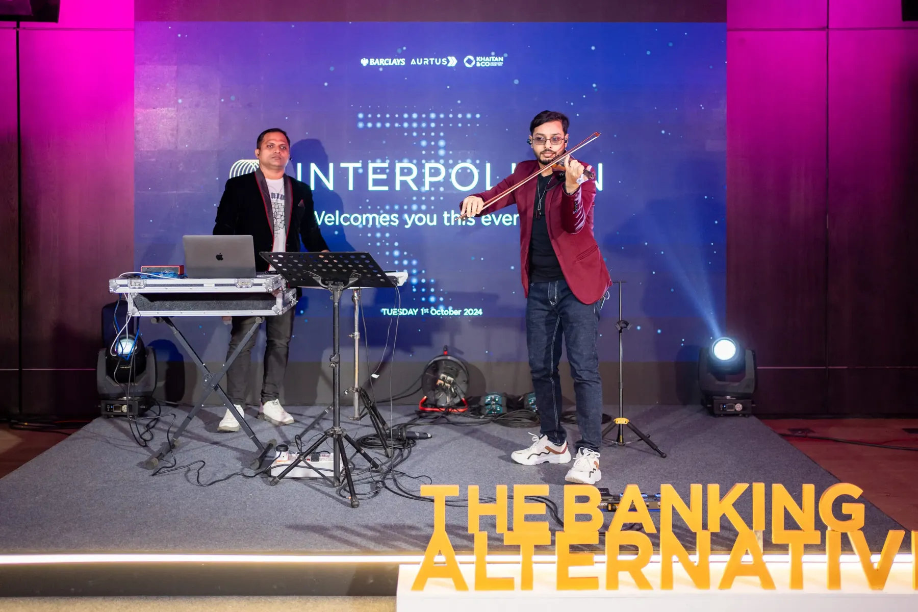 A violinist and keyboardist perform on stage before a Barclays Aurtus branded backdrop.