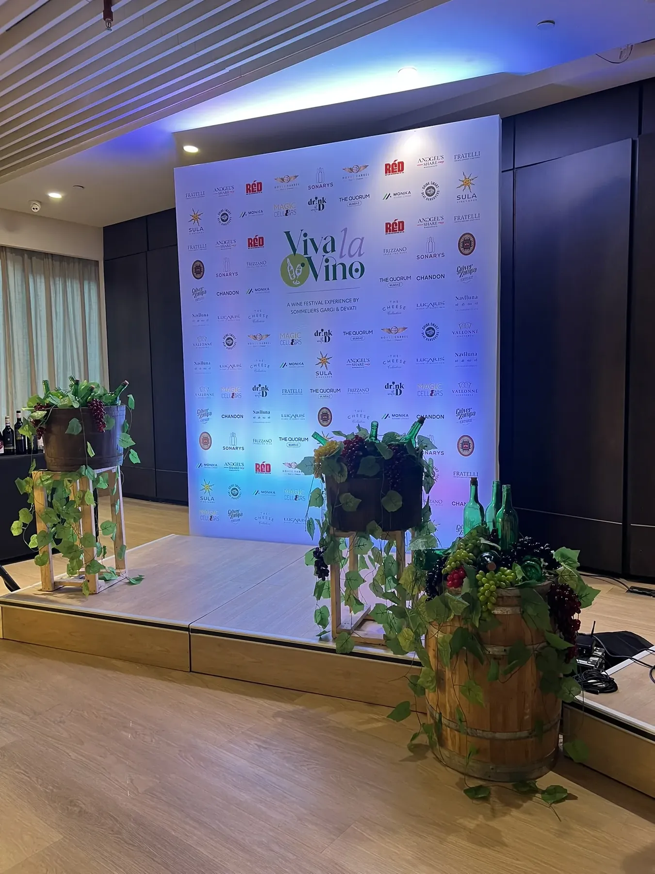 A Viva La Vino sponsor backdrop with wine barrels and grape decorations on stage.