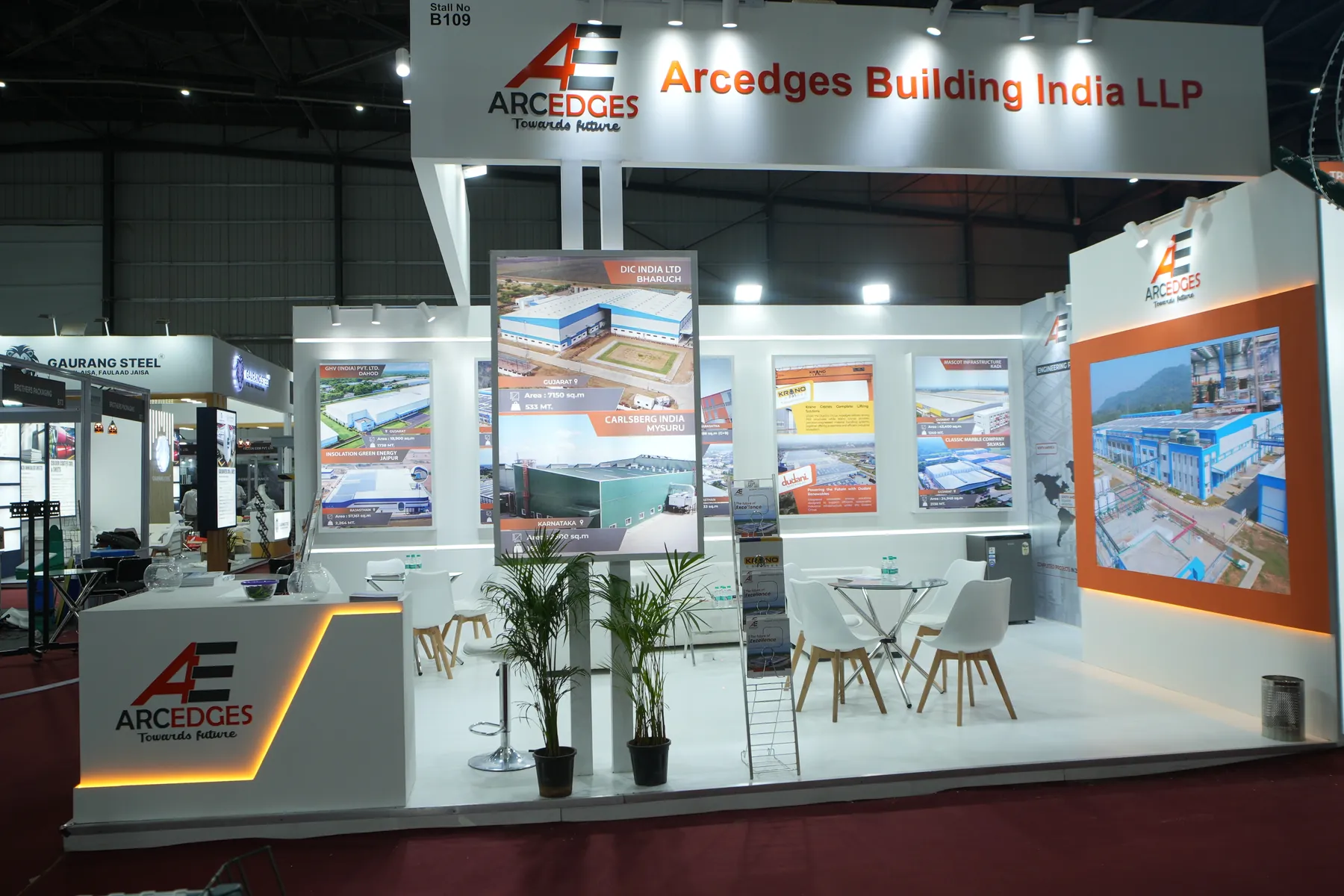 An Arcedges Building India LLP exhibition stall with lit project panels and reception desk.