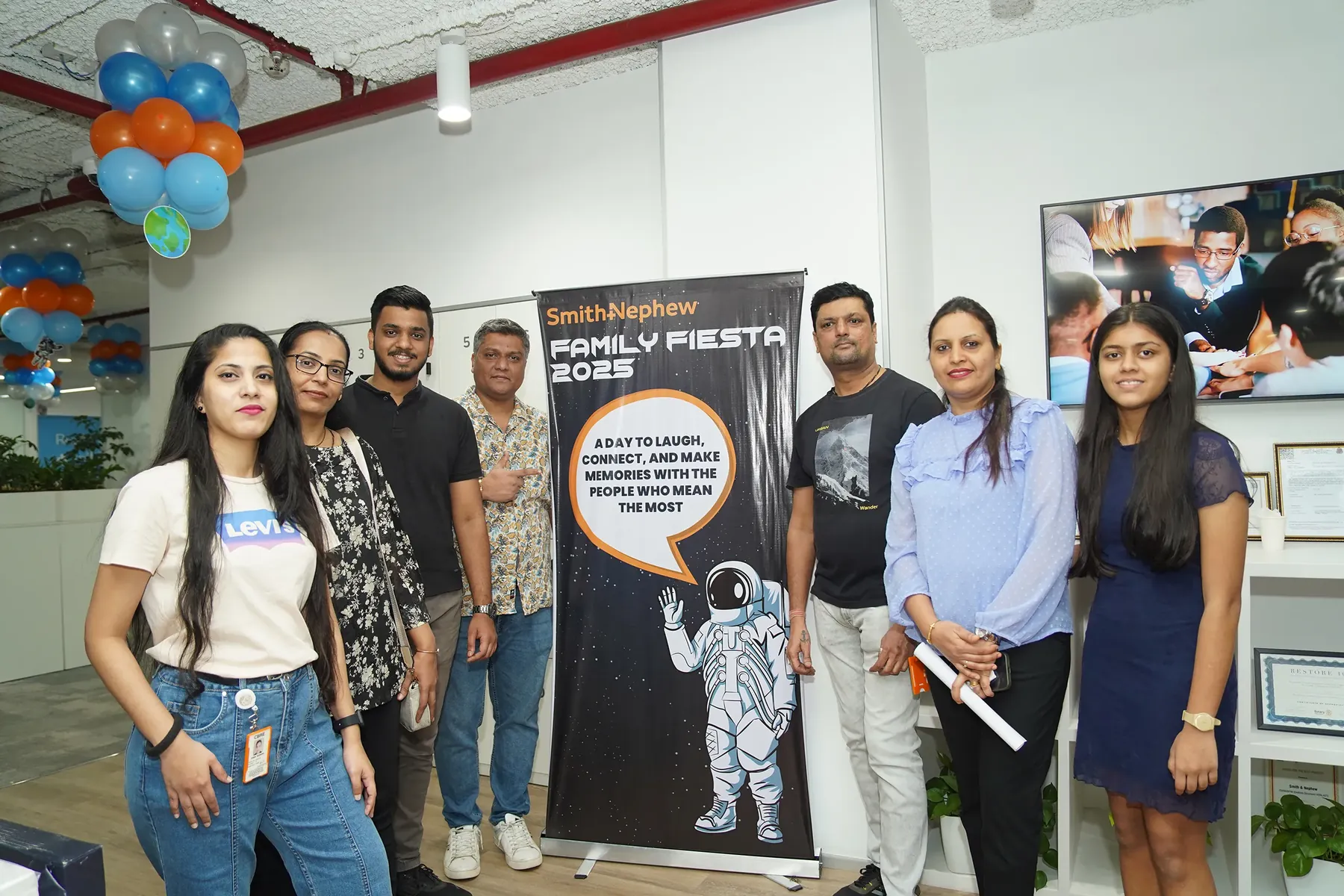 A group of people posing beside a Smith and Nephew Family Fiesta 2025 standee.