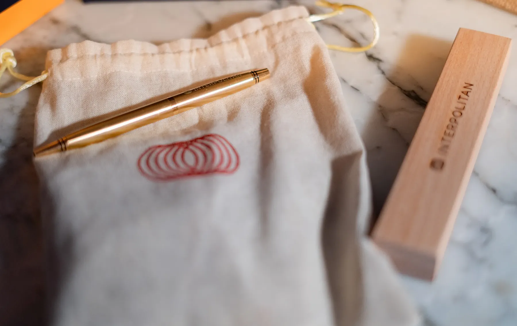An Interpolitan-branded gold pen, cloth pouch and wooden box on marble.