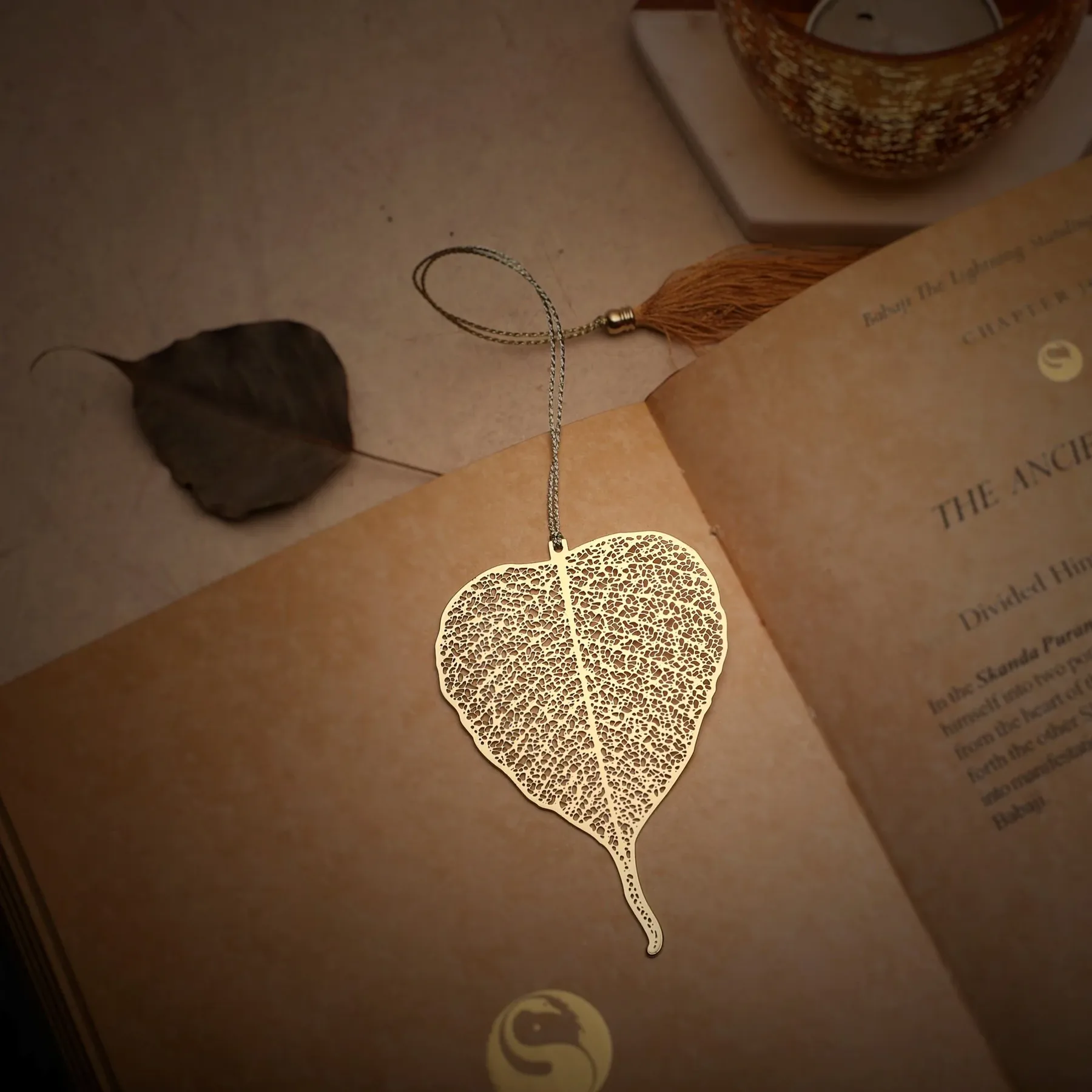 A golden filigree peepal-leaf bookmark with a tassel resting on an open book.