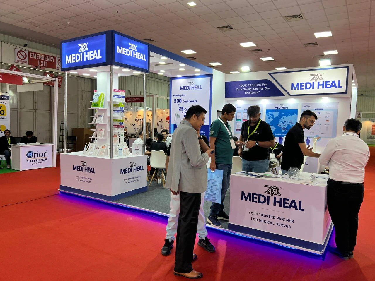 Businessmen networking at the reception counter of the Medi Heal exhibition booth.