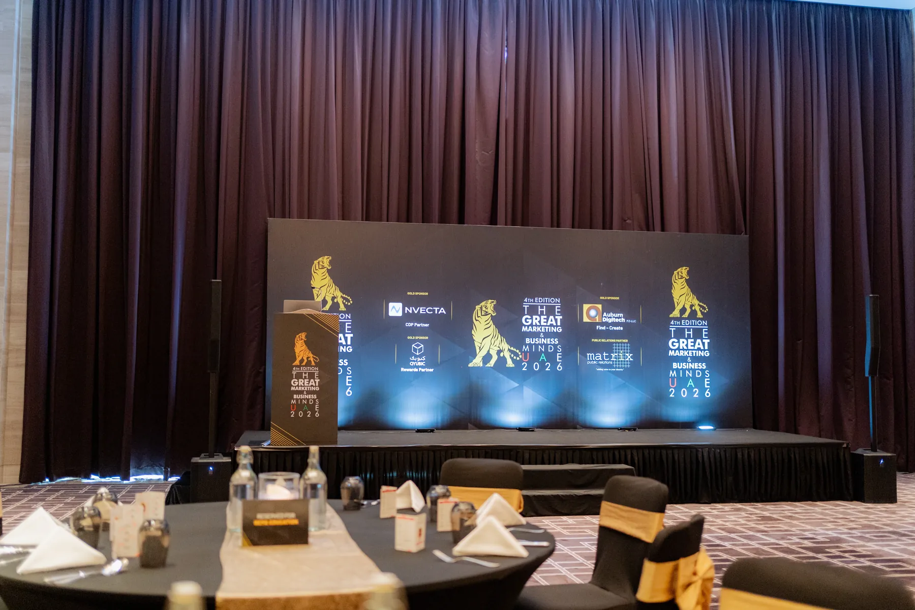 A hotel ballroom awards stage with a golden-lion LED backdrop and banquet tables set for a gala.