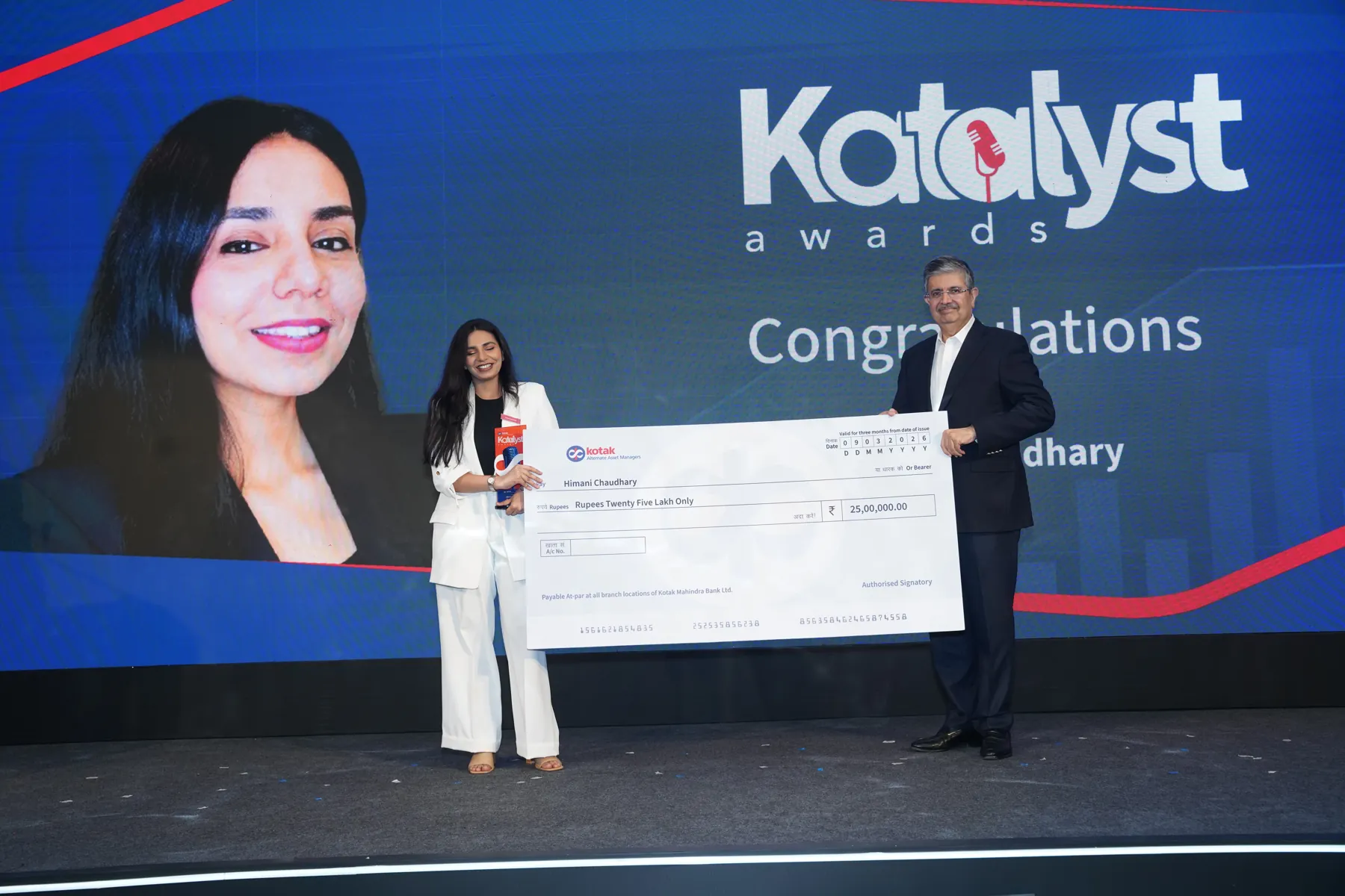 A woman in a white suit receives an award and oversized cheque on stage at the Katalyst Awards.
