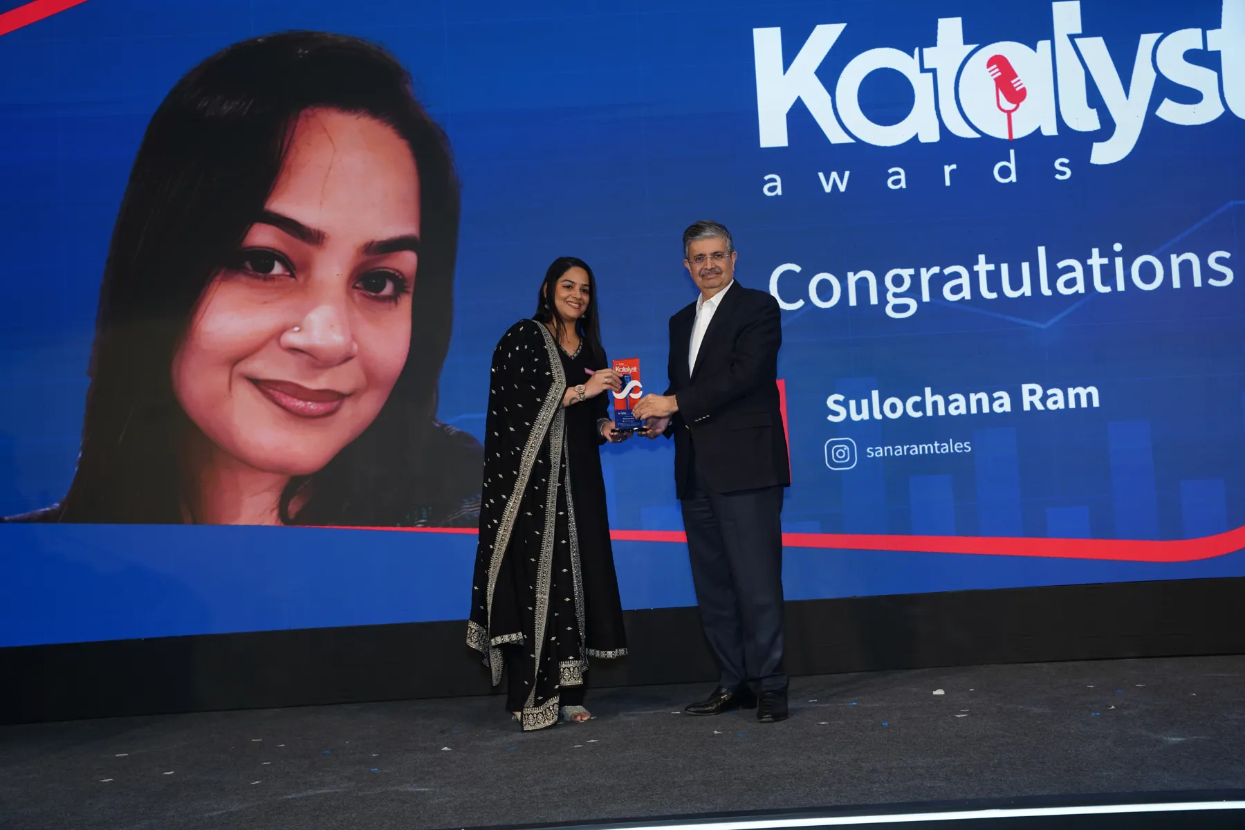 A woman receives an award on stage from a presenter at the Katalyst Awards.