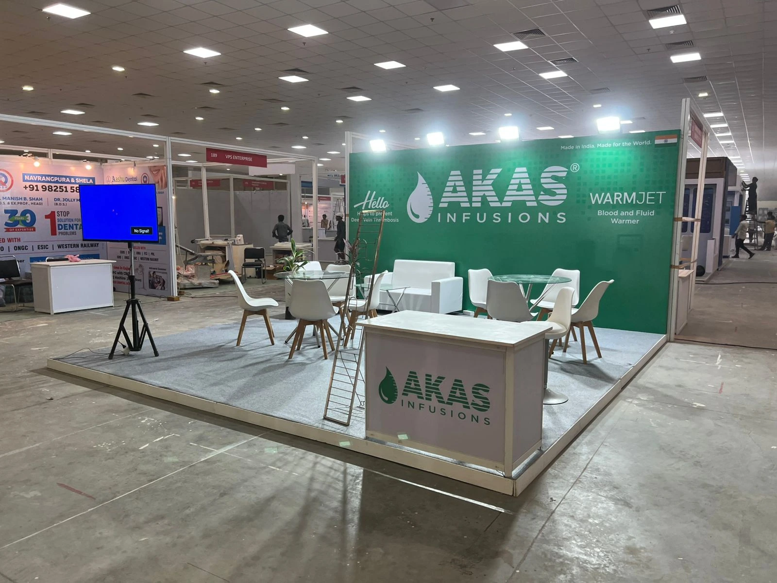 The AKAS Infusions green-and-white exhibition booth with lounge seating and a display screen.