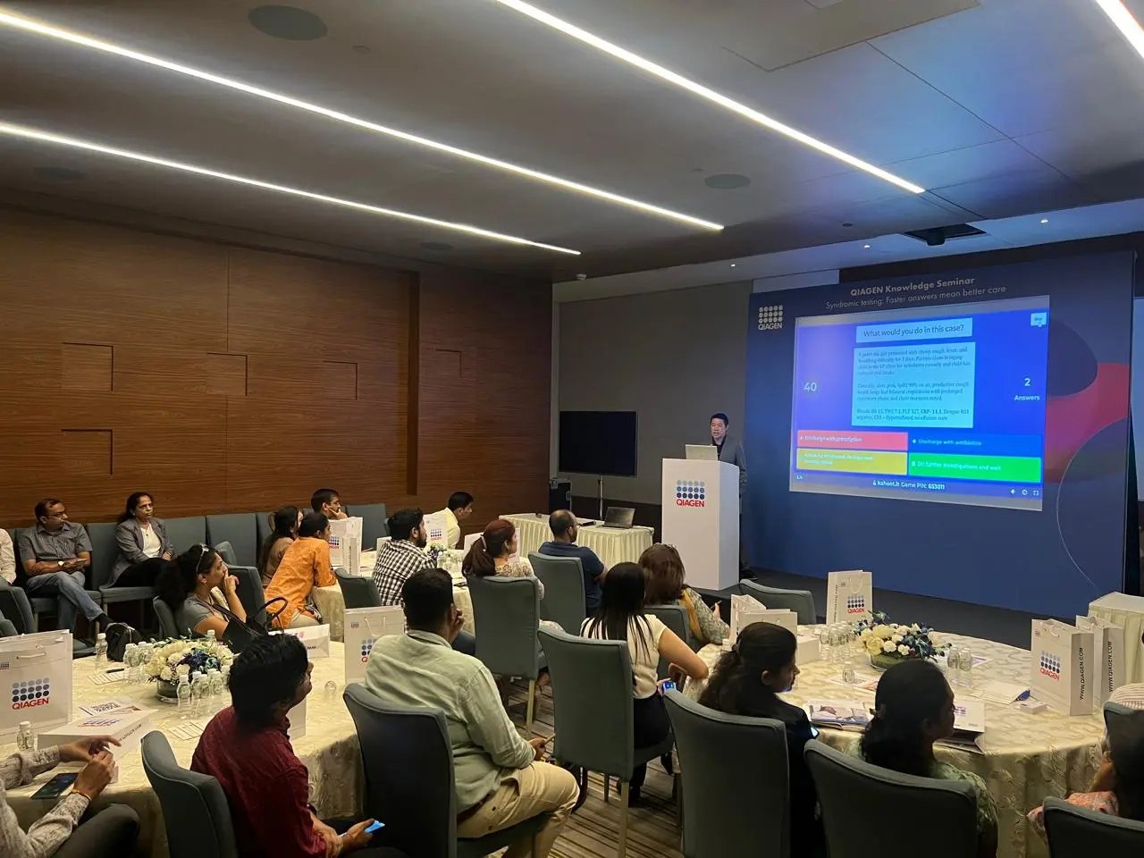 An audience seated at round tables watching a speaker at the QIAGEN Knowledge Seminar.