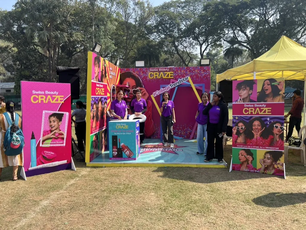 Purple-shirted staff pose at the colourful Swiss Beauty Craze booth on an outdoor field.